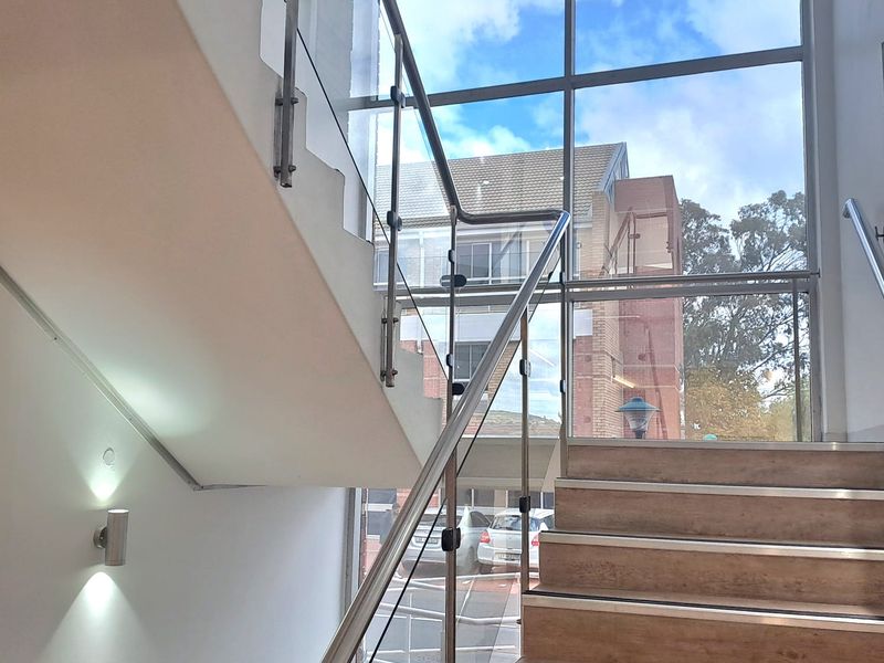 Modern office entrance featuring a staircase with glass balustrades, stainless steel handrails, and large windows providing ample natural light.
