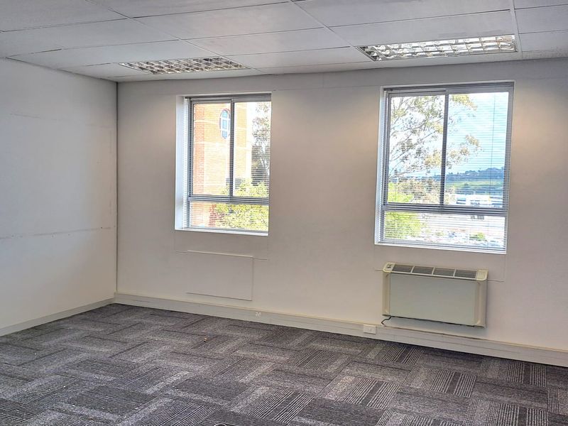 A vacant office space featuring carpet tiles, a suspended ceiling with recessed lighting, and a wall-mounted air conditioning unit.