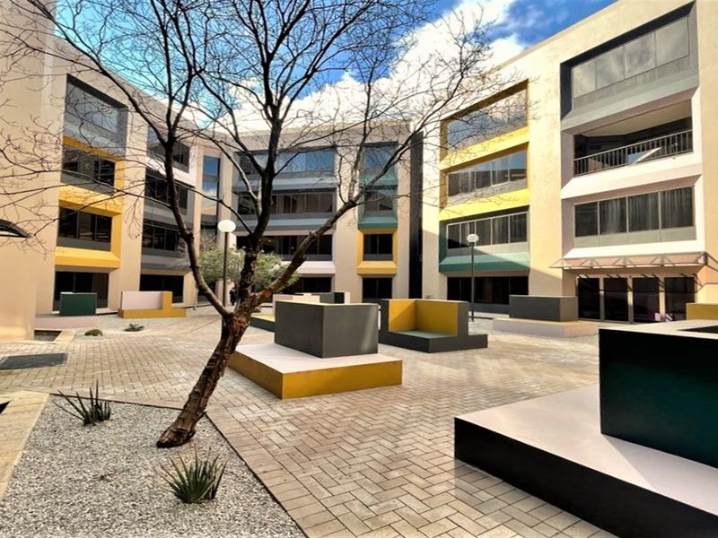 A modern office complex courtyard featuring paved walkways, built-in concrete seating areas, and multi-story building facades with large glass windows.
