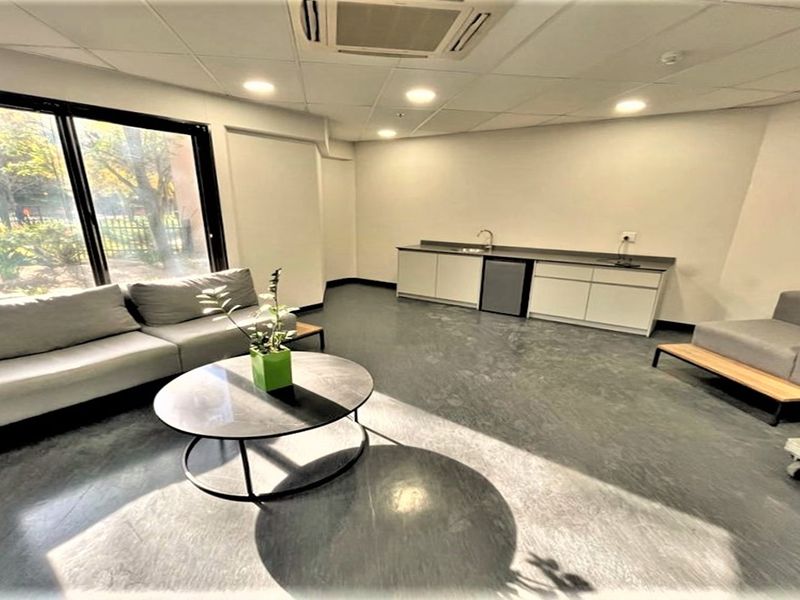 Modern office space featuring a built-in kitchenette, recessed lighting, suspended ceiling, and large sliding glass doors providing ample natural light.