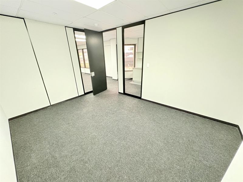 A clean, empty office space featuring neutral carpet flooring, a suspended ceiling, and modern glass partition walls providing a professional work environment.