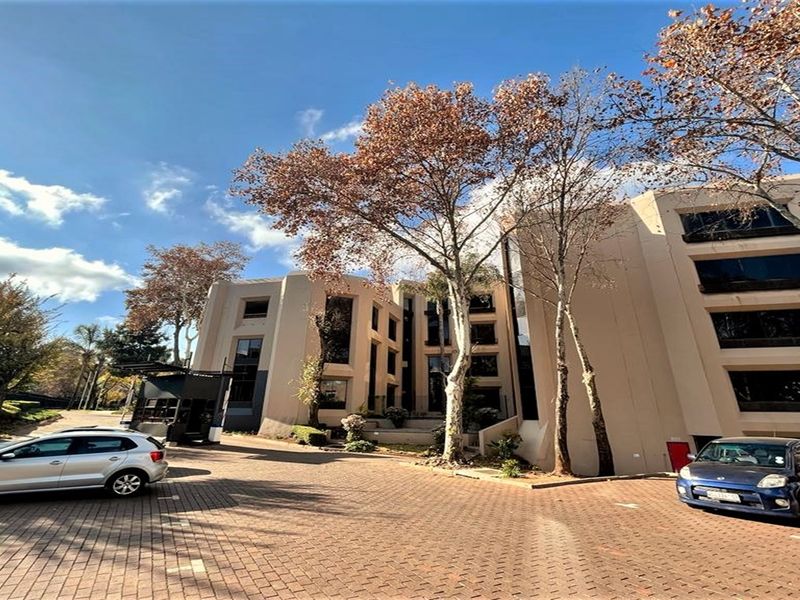 A wide-angle view of a multi-story office building facade featuring a paved driveway and mature trees.