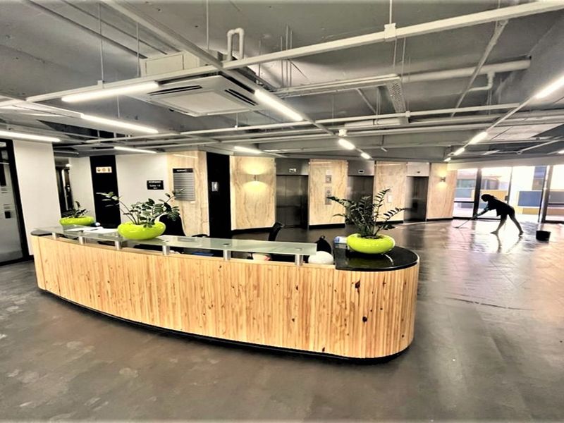 Modern office reception area featuring a curved wooden desk, exposed industrial-style ceiling, and integrated elevator access.