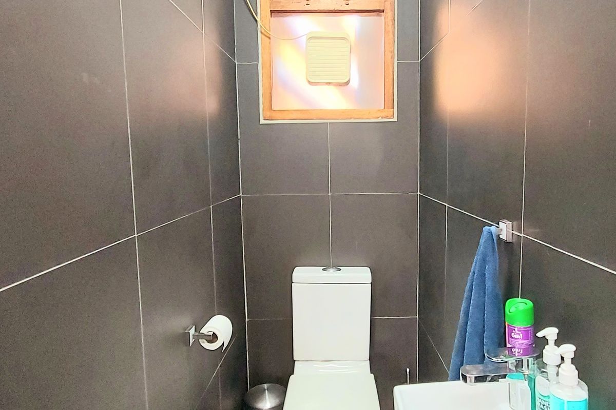 Compact bathroom featuring dark floor-to-ceiling wall tiles, a modern white toilet, and a wall-mounted basin.