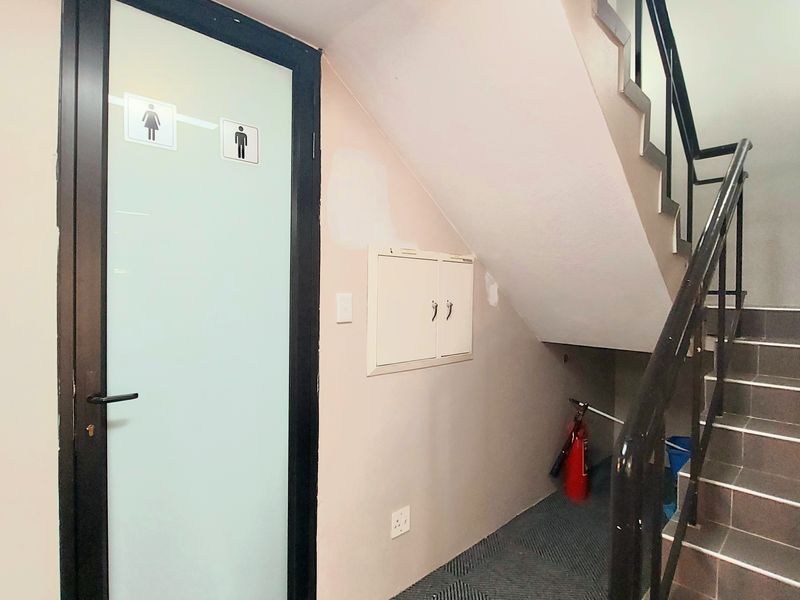 Interior hallway featuring a staircase with metal railings, a restroom access door, and a built-in utility cabinet.