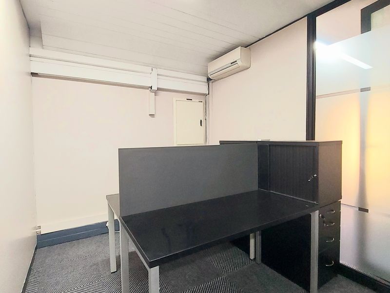 A functional office space featuring patterned carpeting, a wall-mounted air conditioning unit, and a glass partition wall.