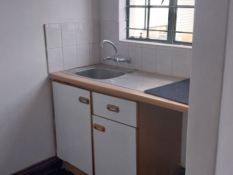A functional scullery or utility area featuring a stainless steel sink, tiled splashback, and built-in cabinetry with a window for natural light.
