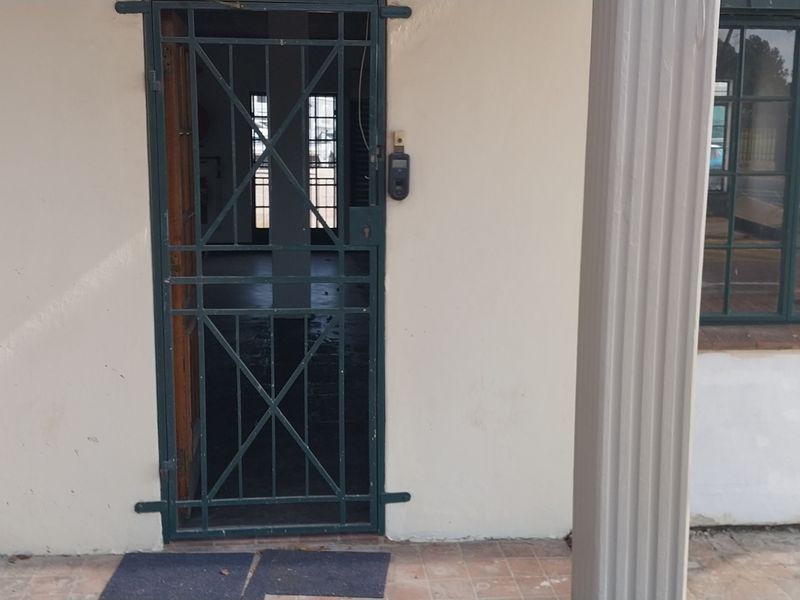 Entrance area featuring a security gate, fluted columns, and steel frame windows, showing signs of wear on the exterior wall finish.