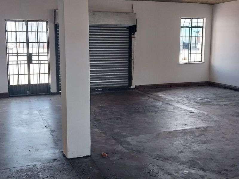Spacious industrial utility area featuring a roller shutter door, security gate, concrete flooring, and integrated fire safety equipment.