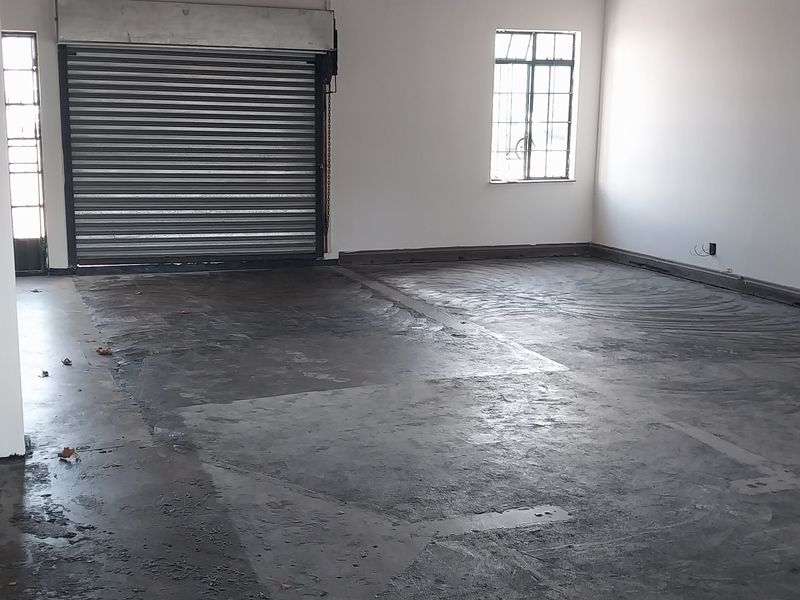 Spacious industrial garage area featuring a roller shutter door, concrete flooring, and integrated fire safety equipment, suitable for storage or workshop use.