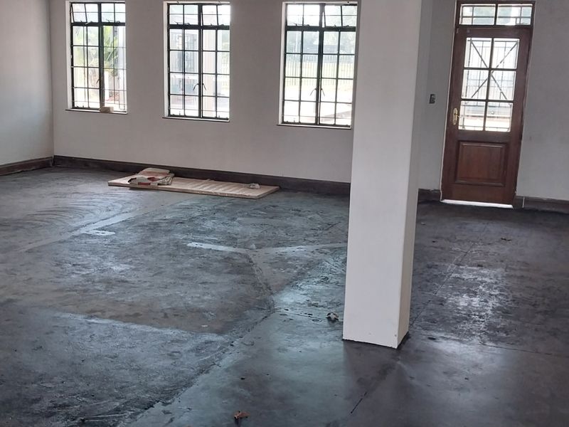 Spacious open-plan industrial area featuring concrete flooring, multiple steel-framed windows, and a timber-framed glass entrance door.
