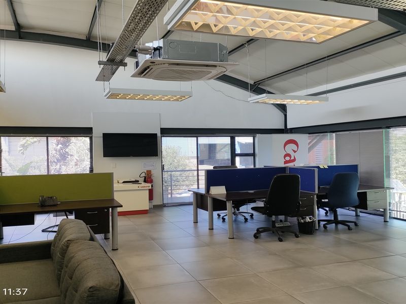 Spacious open-plan industrial office featuring high ceilings with exposed steel trusses, modern cassette air conditioning, and large windows providing ample natural light.
