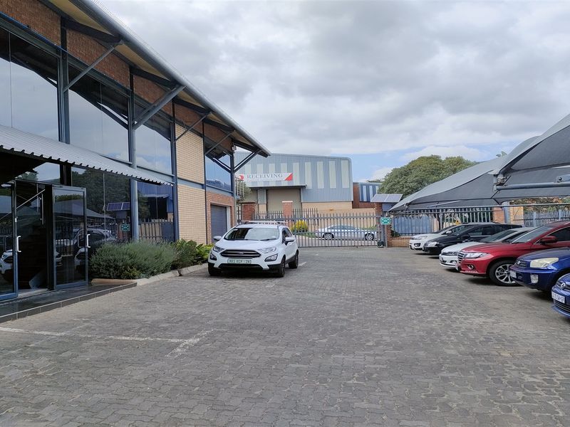 Industrial property exterior featuring a paved parking area with shade cloth structures, modern steel and glass facade, and secure perimeter fencing.