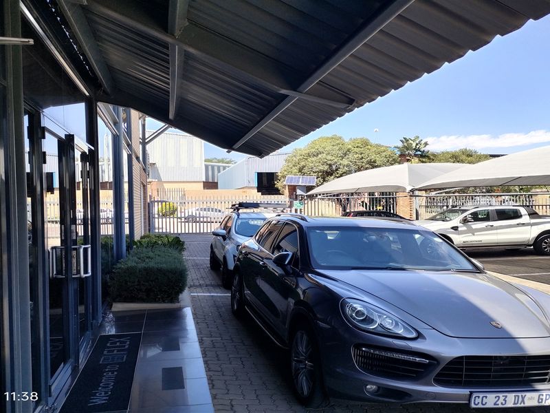 Front exterior view of the industrial property featuring a glass entrance, metal awning, paved driveway, and covered parking area.