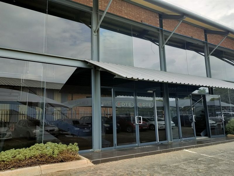 Modern industrial building facade featuring a large glass curtain wall, steel structural framing, and a protective metal awning over the main entrance.