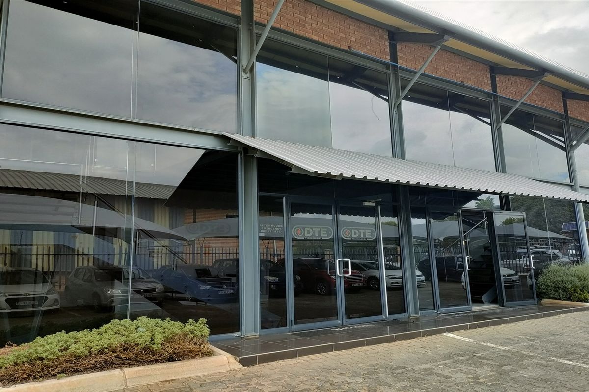 Modern industrial building facade featuring a large glass curtain wall, steel structural framing, and a protective metal awning over the main entrance.