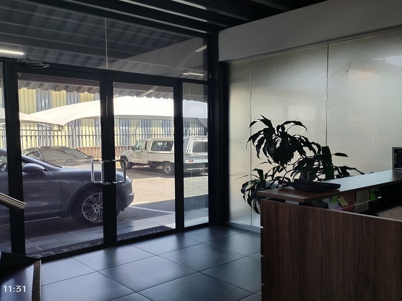 Modern industrial entrance area featuring glass double doors, tiled flooring, and a built-in reception desk with frosted glass partitioning.
