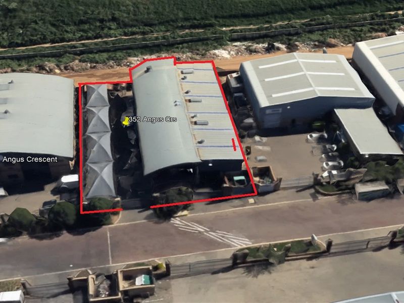 Aerial view of an industrial property featuring a metal-roofed warehouse building with skylights and surrounding paved access areas.
