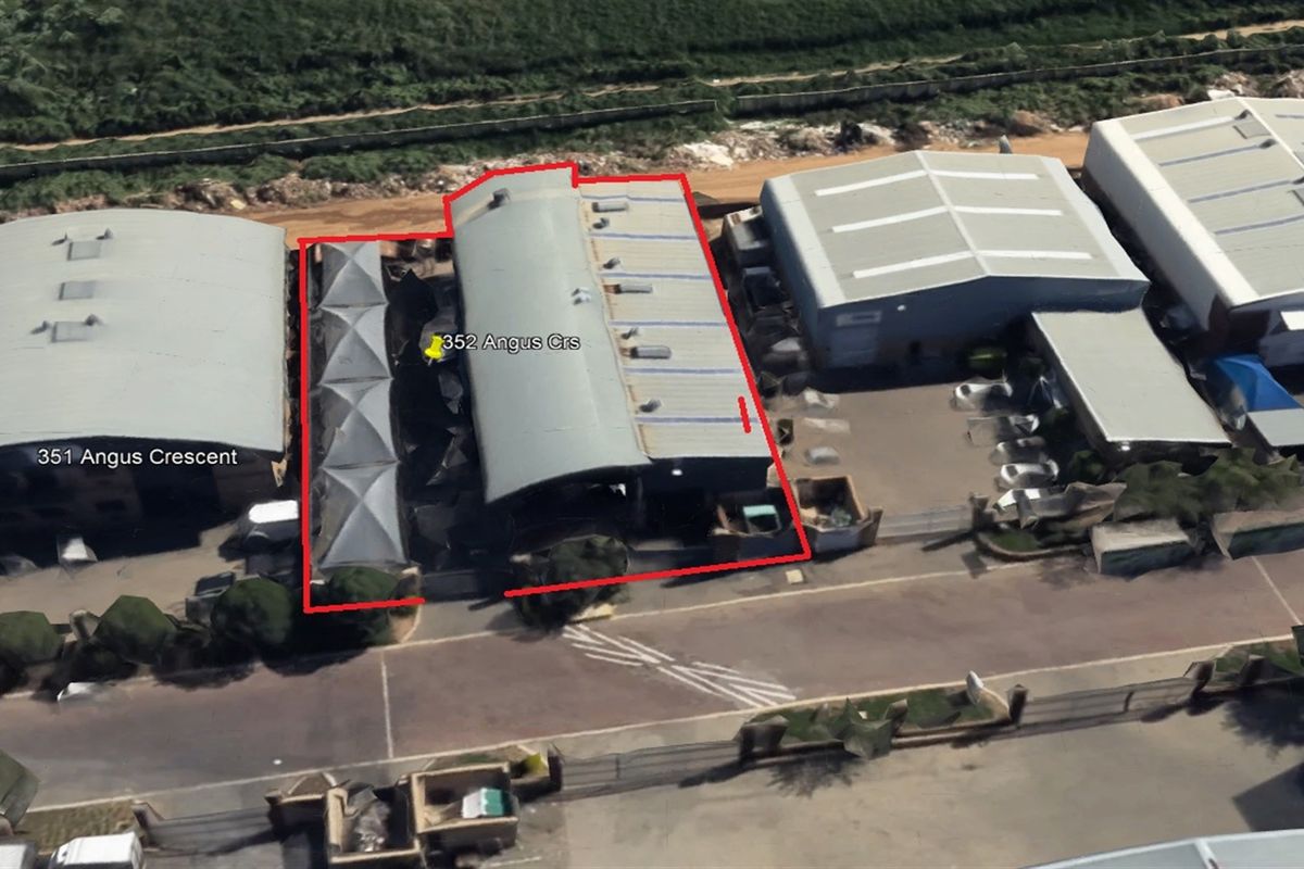 Aerial view of an industrial property featuring a metal-roofed warehouse building with skylights and surrounding paved access areas.