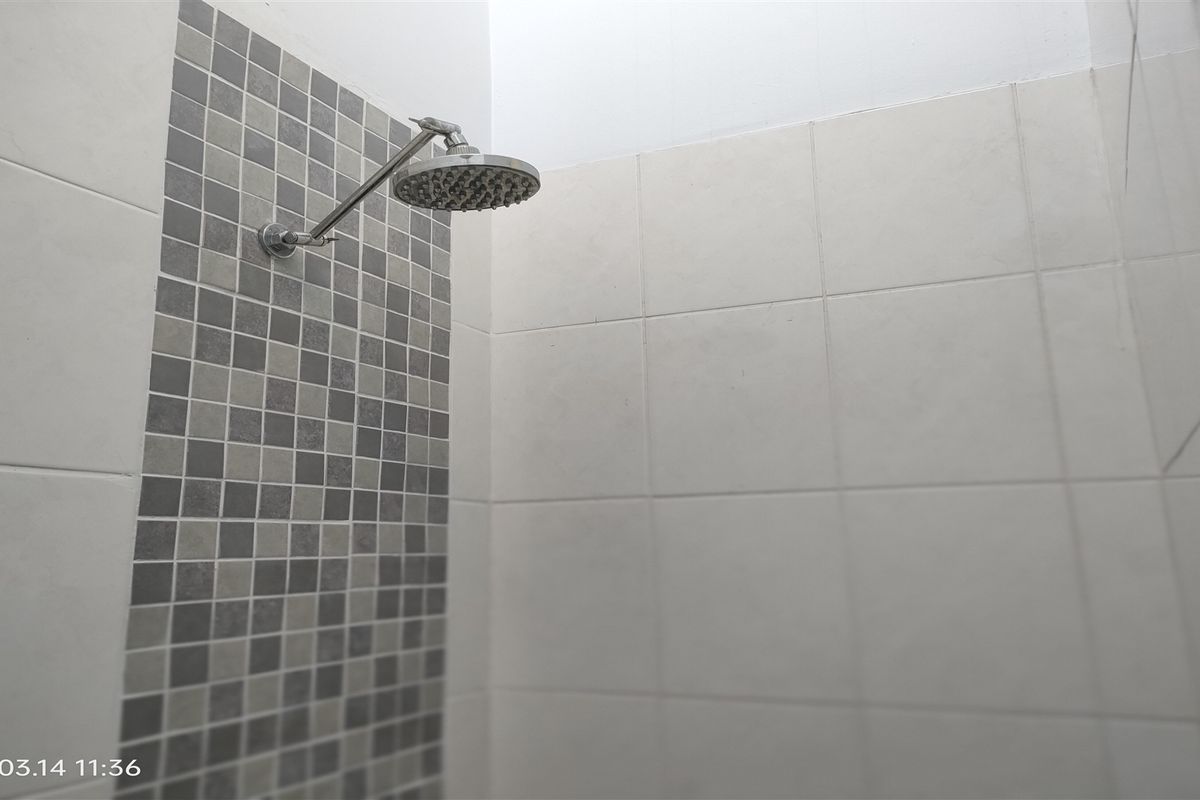 A clean shower enclosure featuring a modern shower head, accented with grey mosaic tiling and neutral ceramic wall tiles.