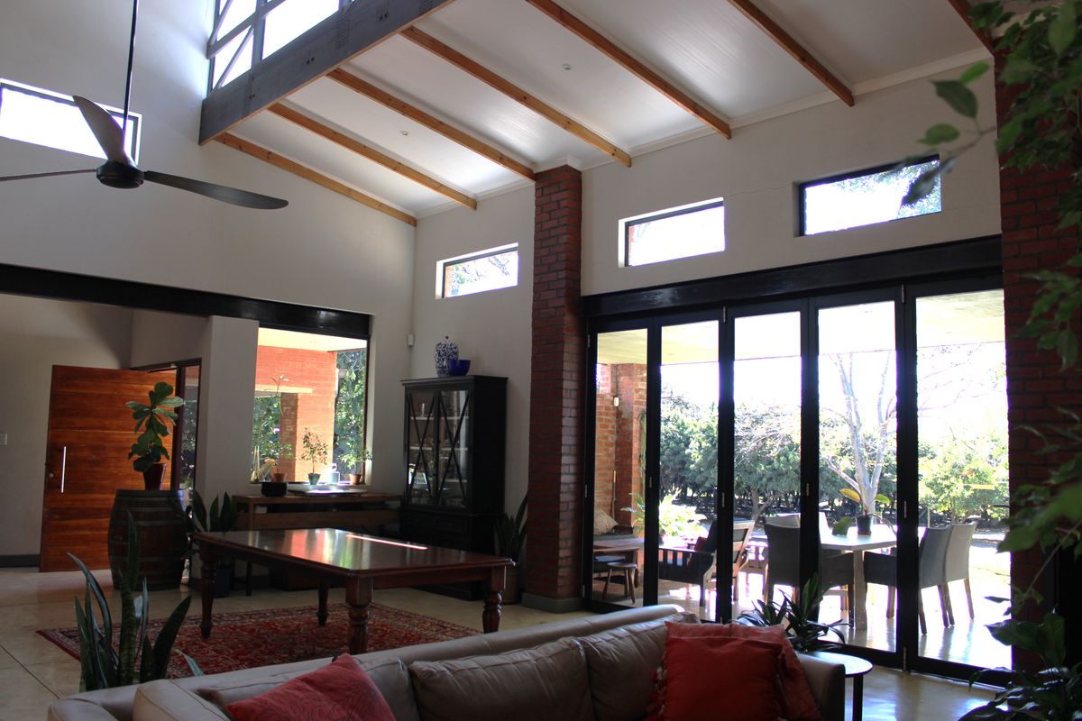 Spacious living area featuring high vaulted ceilings with exposed timber beams, brick accents, and large bi-fold doors opening to the outdoor patio.