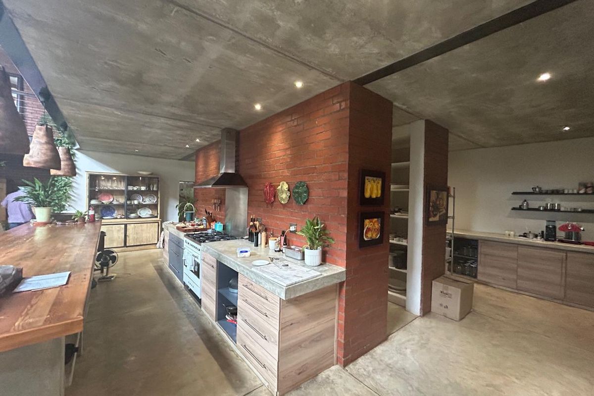Modern industrial-style kitchen featuring exposed concrete ceilings, brick feature walls, concrete countertops, and a spacious walk-in pantry area.