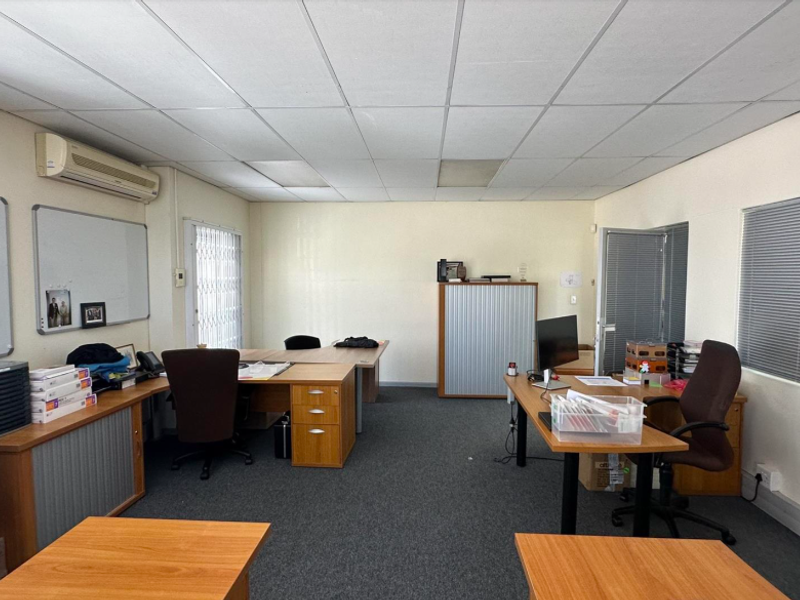 A functional office space featuring carpeted flooring, a suspended ceiling, and a wall-mounted air conditioning unit.