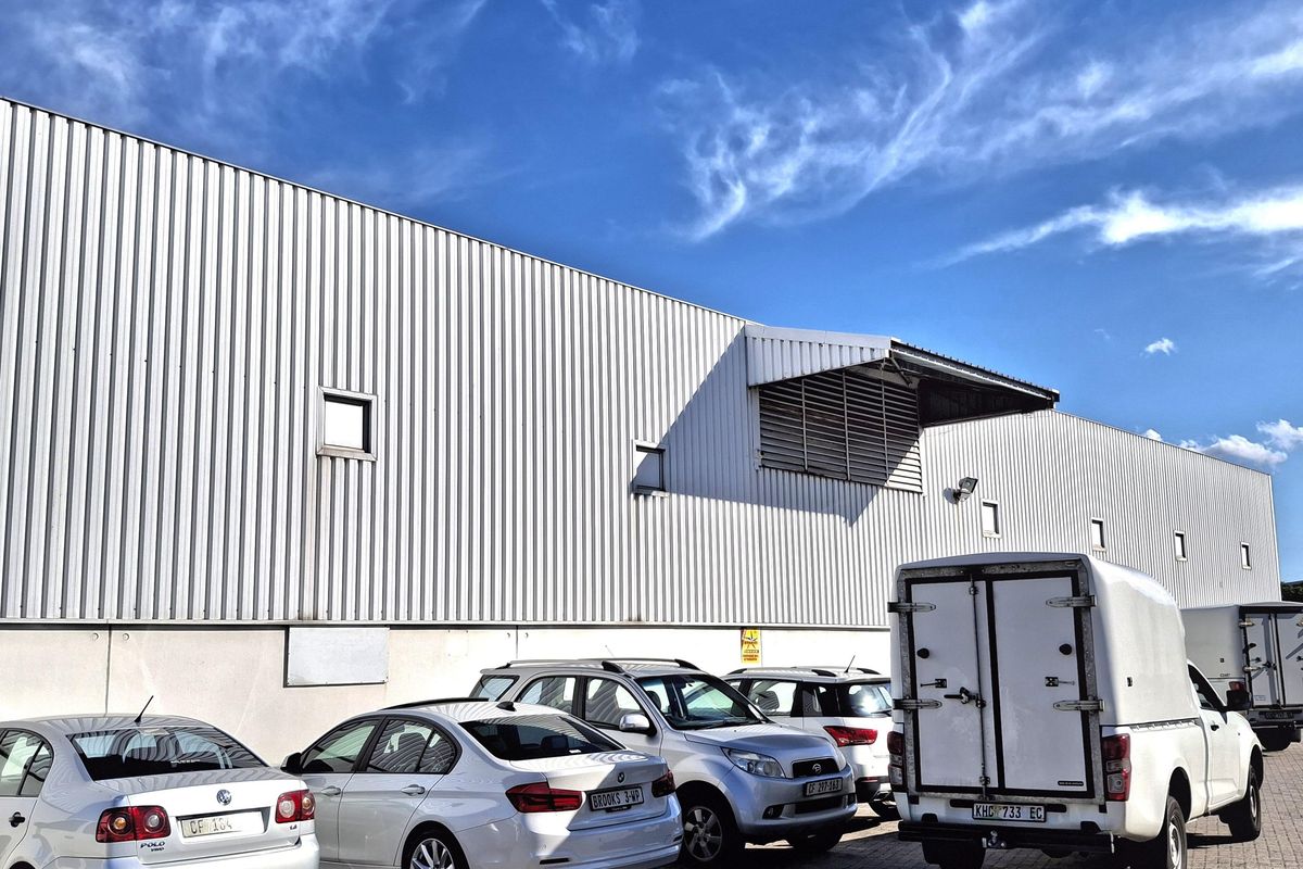 Exterior view of an industrial warehouse facility featuring corrugated metal cladding, a concrete base, and a paved parking area.
