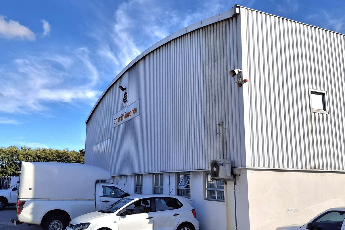 Exterior view of an industrial warehouse facility featuring corrugated metal cladding, external security lighting, and an integrated air conditioning unit with dedicated parking.