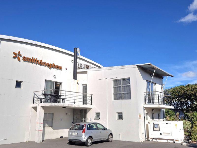 Rear elevation of an industrial facility featuring white painted masonry, metal balconies, external HVAC units, and a dedicated generator enclosure within a paved parking area.