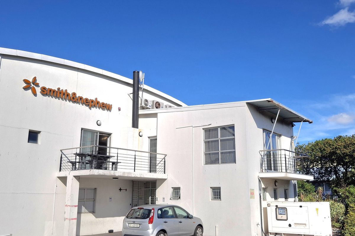 Rear elevation of an industrial facility featuring white painted masonry, metal balconies, external HVAC units, and a dedicated generator enclosure within a paved parking area.