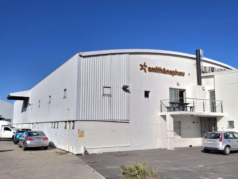 Exterior view of an industrial warehouse facility featuring corrugated metal cladding, a small balcony, and dedicated asphalt parking space.