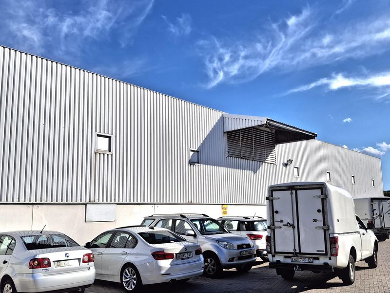 Exterior view of an industrial warehouse facility featuring corrugated metal cladding, a concrete base, and a paved parking area.