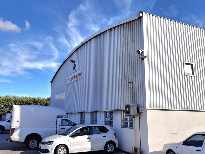 Exterior view of an industrial warehouse facility featuring corrugated metal cladding, external security lighting, and an integrated air conditioning unit with dedicated parking.