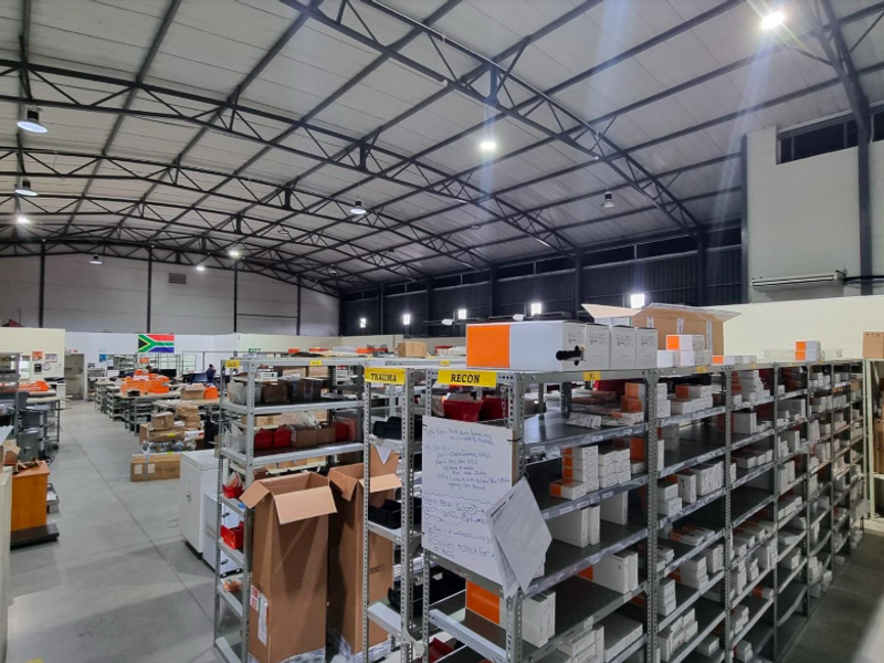 Spacious industrial warehouse facility featuring high-clearance exposed steel truss roofing, polished concrete flooring, and extensive integrated metal shelving for storage.