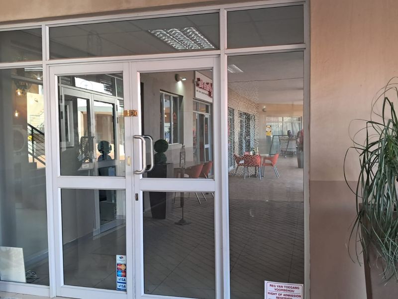 Main entrance featuring aluminium-framed glass double doors with sidelights and transom windows, providing clear visibility into the retail space.