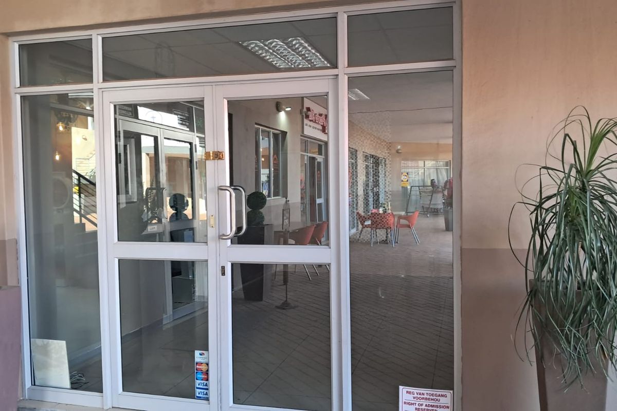 Main entrance featuring aluminium-framed glass double doors with sidelights and transom windows, providing clear visibility into the retail space.