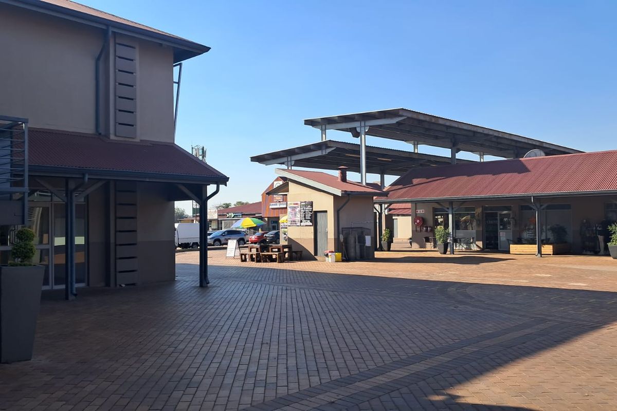 A well-maintained retail courtyard featuring paved walkways, covered storefront areas, and modern steel-framed roofing structures.