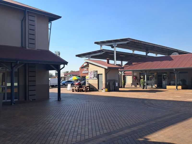 A well-maintained retail courtyard featuring paved walkways, covered storefront areas, and modern steel-framed roofing structures.