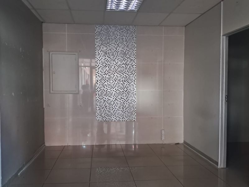 An empty utility or commercial space featuring tiled flooring, a drop ceiling with recessed lighting, and a decorative mosaic wall accent.