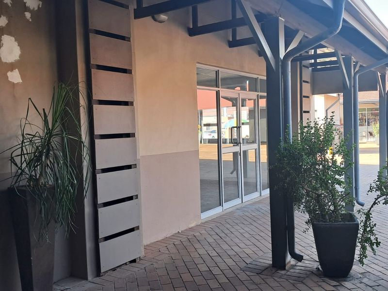 Front entrance of a retail unit featuring a covered walkway, paved flooring, and aluminium-framed glass doors.