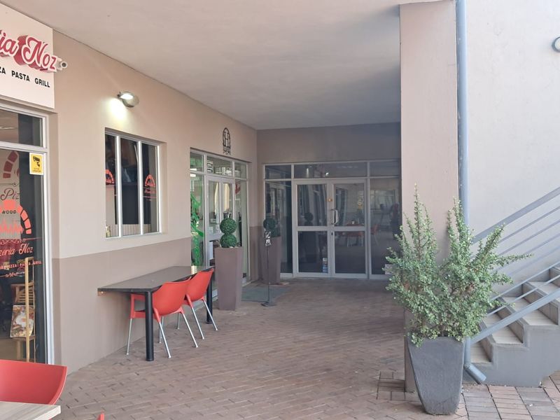 Covered outdoor patio area at a retail pizzeria, featuring paved flooring, access to an external staircase, and glass storefront entrance doors.