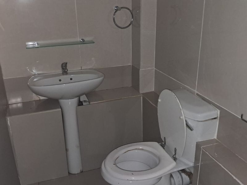 A functional bathroom featuring a pedestal washbasin, toilet, and neutral wall tiling with integrated fixtures.
