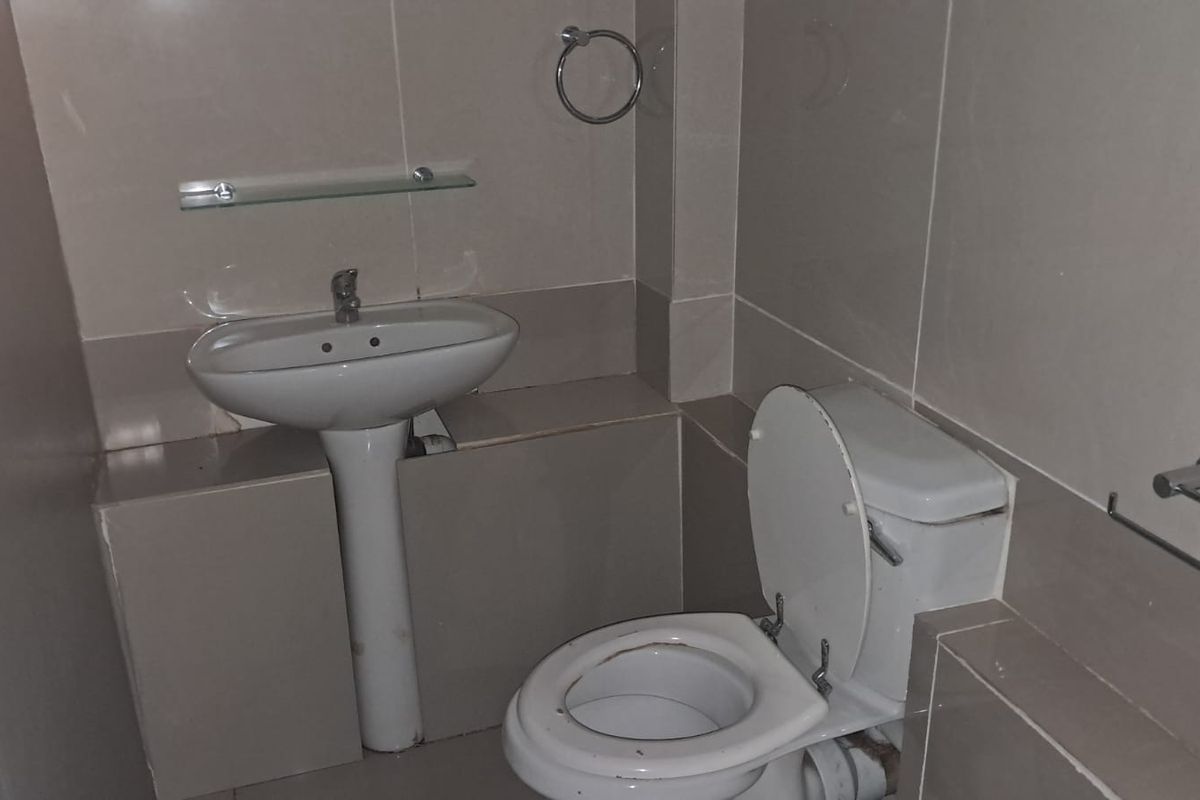 A functional bathroom featuring a pedestal washbasin, toilet, and neutral wall tiling with integrated fixtures.