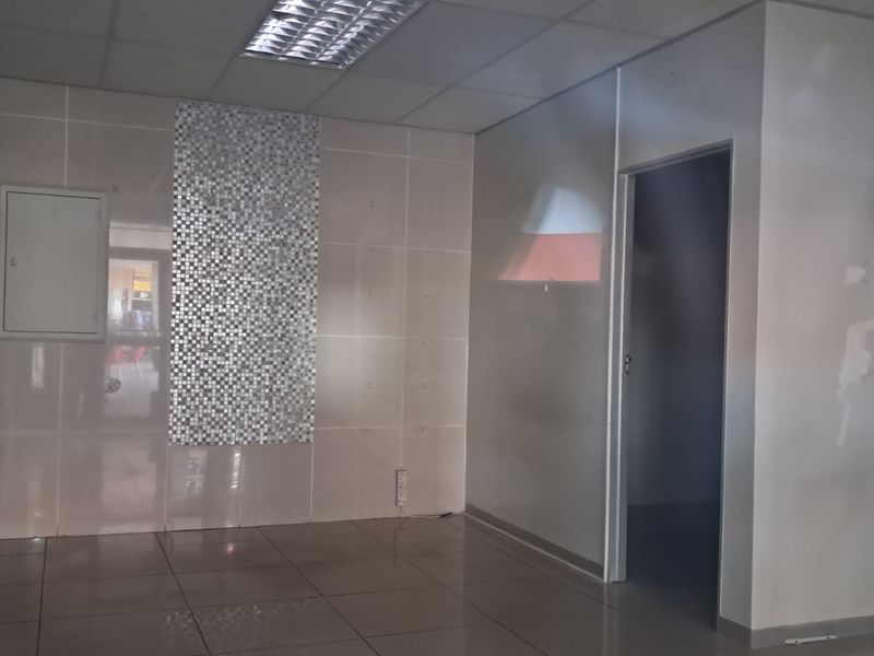 An empty commercial office space featuring tiled flooring, wall cladding with a mosaic feature panel, and a suspended ceiling with recessed lighting.
