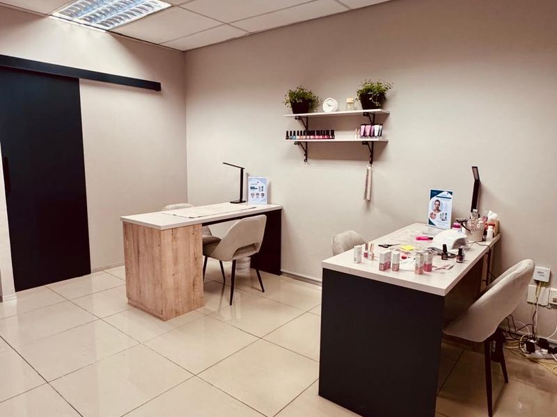 A clean, professional office or salon space featuring neutral ceramic floor tiles, a suspended ceiling with recessed lighting, and a functional sliding door.