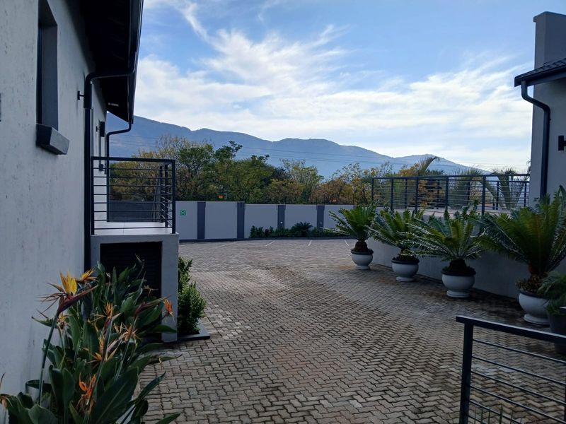 A well-maintained paved driveway and entrance area featuring perimeter walling, metal railings, and mountain views.