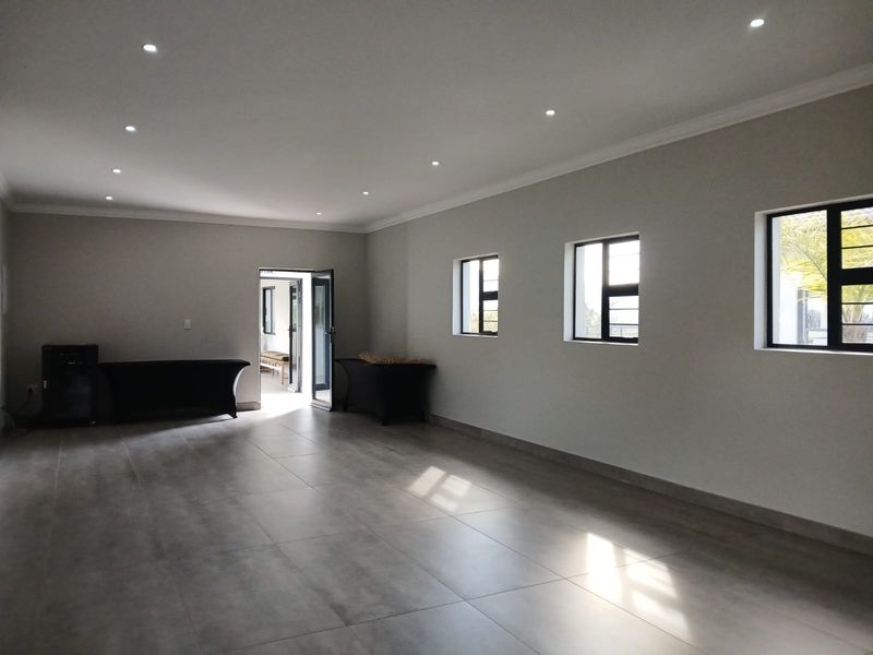 A spacious, empty living area featuring neutral tiled flooring, recessed downlighting, and large windows that provide ample natural light.