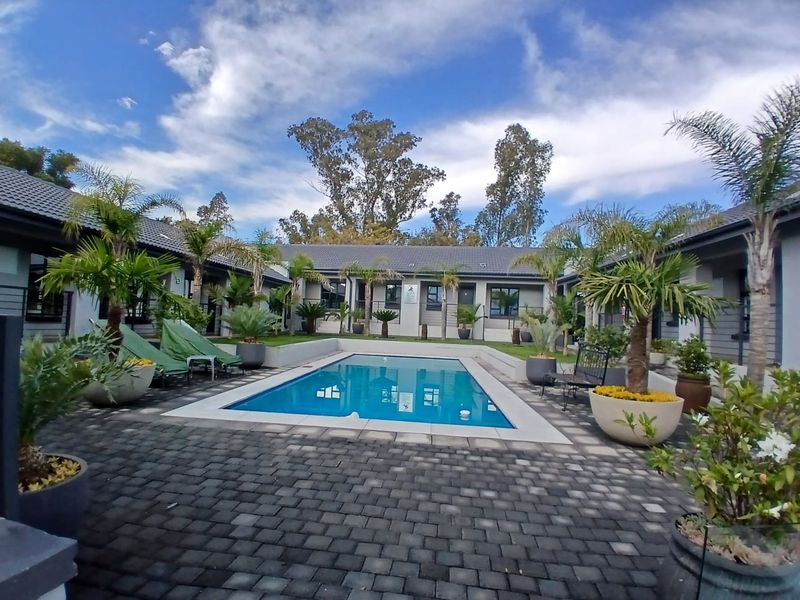 A well-maintained central swimming pool area surrounded by paved decking and guest house units with tiled roofing.