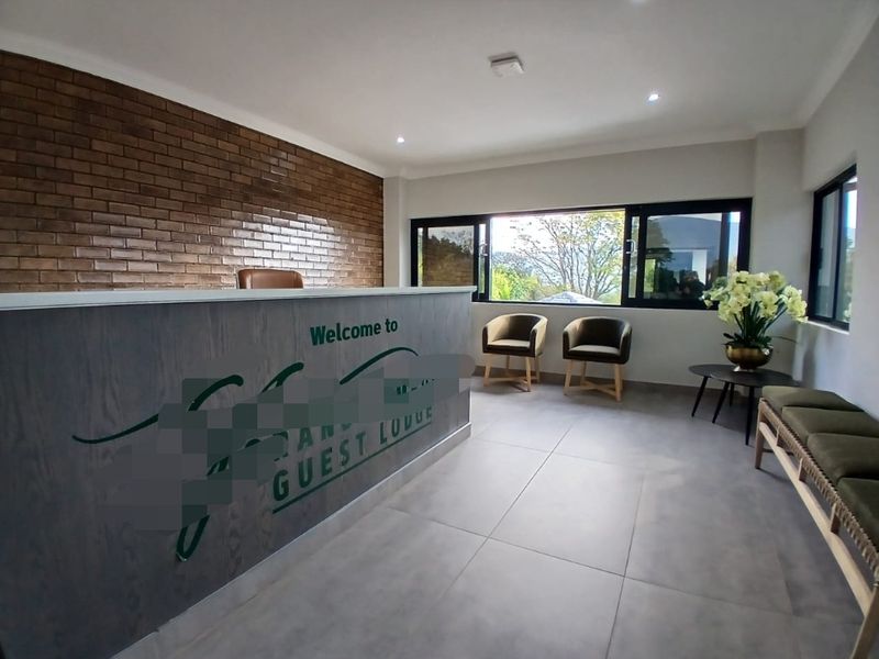 A bright and modern guest house reception area featuring a built-in desk, an exposed brick feature wall, and large windows with natural light.
